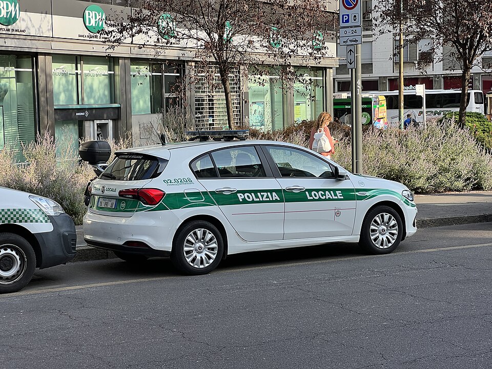 White and green Milan municipal police car parked on a city street.