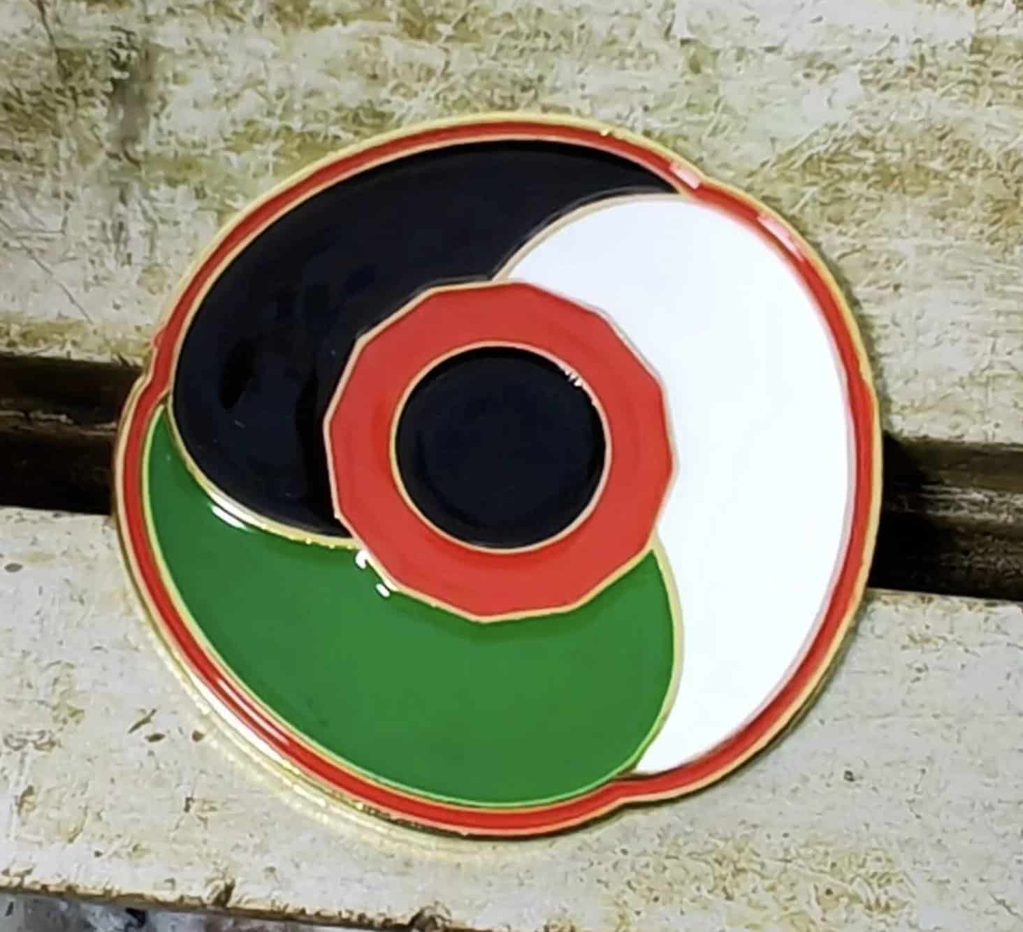 A circular “Palestine Poppy” pin featuring a red poppy at its center, surrounded by the black, white, and green colors of the Palestinian flag.