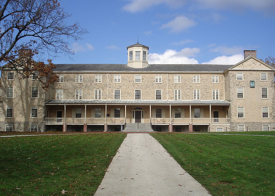 Stone campus building at Haverford College, with a central cupola, covered porch, and walkway across a green lawn.