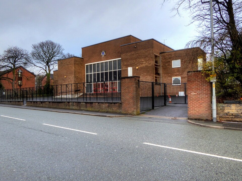 Brick exterior of Heaton Park Hebrew Congregation in Manchester, with a Star of David above its entrance and black perimeter fencing.