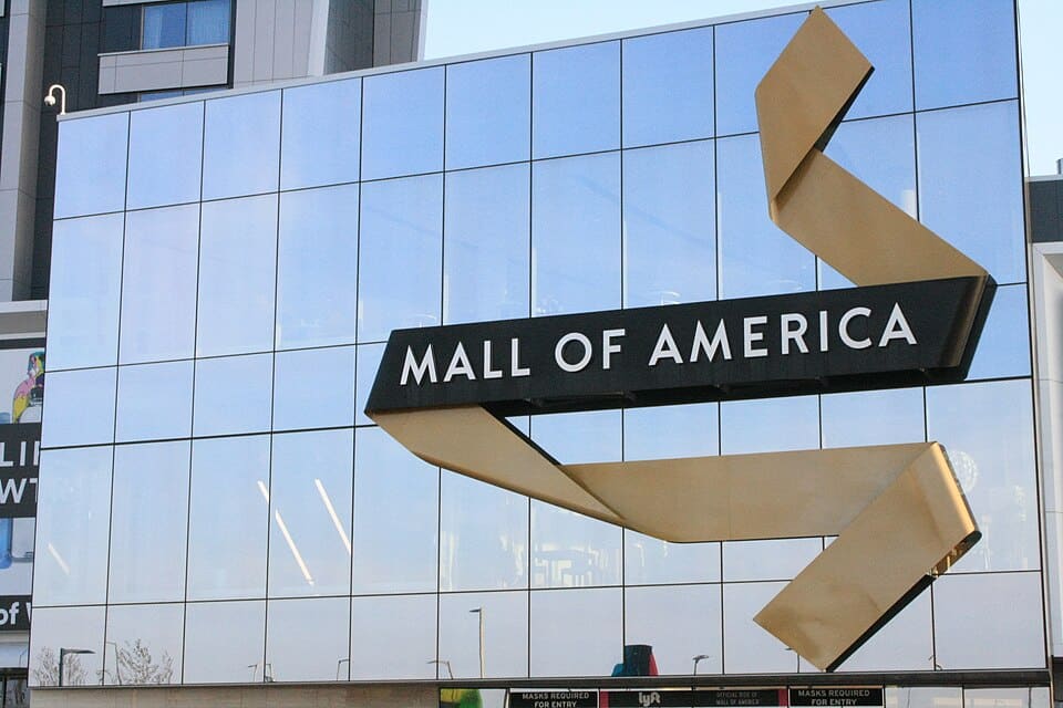 Mall of America sign with a gold ribbon design outside the glass façade in Bloomington, Minnesota.