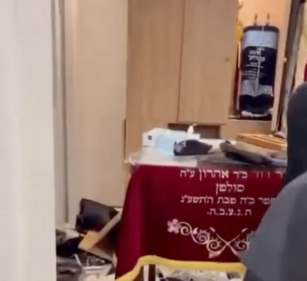 Interior of a Paris synagogue showing scattered belongings and furniture beside a red Torah ark curtain following an apparent break-in.